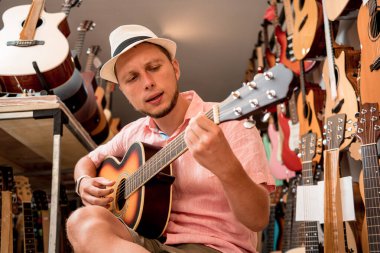 Genç bir müzisyen gitarı gitar dükkanında test ediyor..