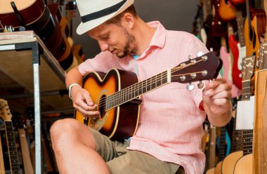 Genç bir müzisyen gitar dükkanında klasik gitar akort ediyor..