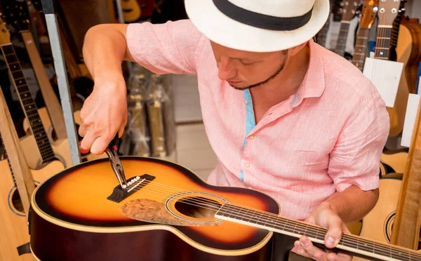 年轻音乐家在吉他手商店里的古典吉他手上变换弦子 — 图库照片