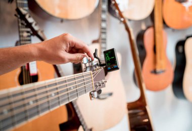 Genç bir müzisyen gitar dükkanında klasik gitar akort ediyor..