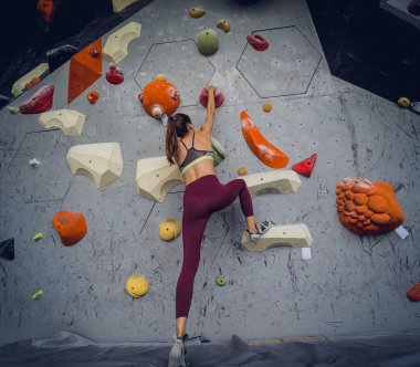 Güçlü bir dişi tırmanıcı renkli tutacakları ve ipleriyle yapay bir duvara tırmanır.