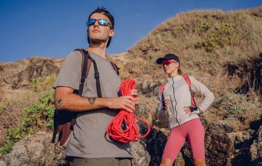 Genç çift, okyanus kıyısındaki dağların zirvesine bir iple tırmanır..