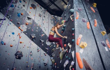 Güçlü bir dişi tırmanıcı renkli tutacakları ve ipleriyle yapay bir duvara tırmanır.