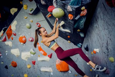 Güçlü bir dişi tırmanıcı renkli tutacakları ve ipleriyle yapay bir duvara tırmanır.