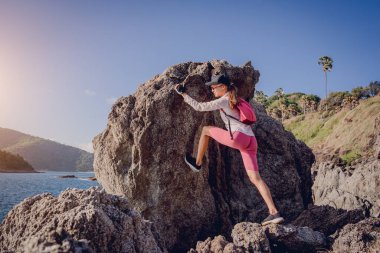 Genç bir kadın okyanusun yakınındaki dağların tepesine tırmanıyor..
