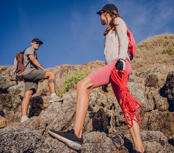 Young couple climbs with a rope to the top in the mountains near the ocean.