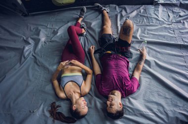 Güçlü bir çift tırmanışçı renkli tutacakları ve ipleriyle yapay duvarın yanında rahatlar.