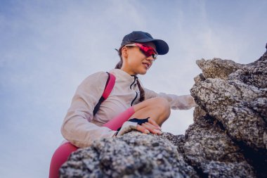 Genç bir kadın okyanusun yakınındaki dağların tepesine tırmanıyor..