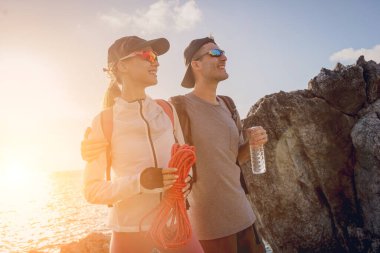 Genç çift, okyanus kıyısındaki dağların zirvesine bir iple tırmanır..