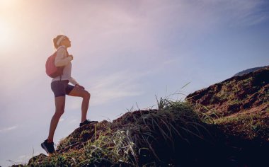 Genç bir kadın okyanusun yakınındaki dağların tepesine tırmanıyor..