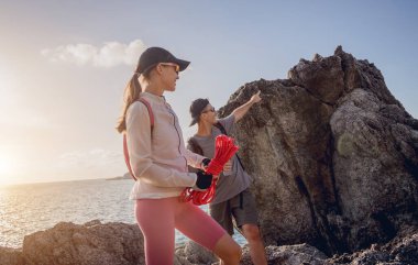 Genç çift, okyanus kıyısındaki dağların zirvesine bir iple tırmanır..