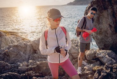 Genç çift, okyanus kıyısındaki dağların zirvesine bir iple tırmanır..