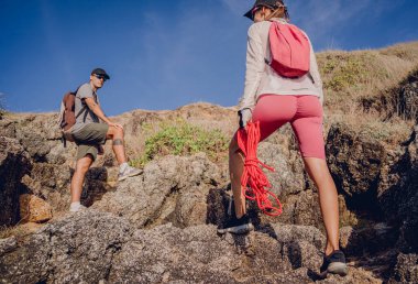 Genç çift, okyanus kıyısındaki dağların zirvesine bir iple tırmanır..