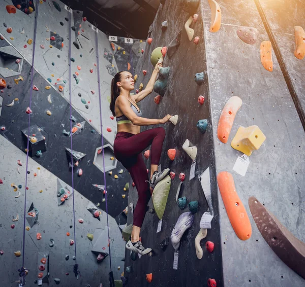 一个强壮的女登山者爬上了用五彩缤纷的抓子和绳索搭成的人造墙 — 图库照片