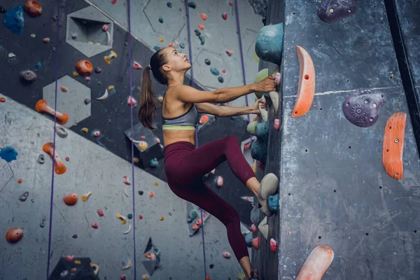 一个强壮的女登山者爬上了用五彩缤纷的抓子和绳索搭成的人造墙 — 图库照片