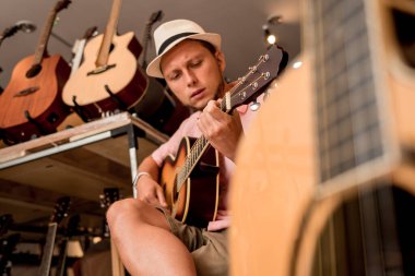 Genç bir müzisyen gitarı gitar dükkanında test ediyor..