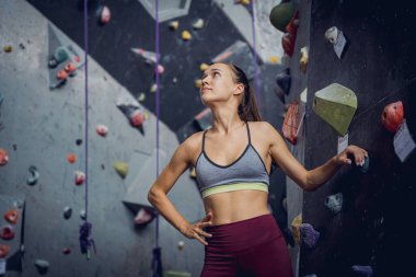 Güçlü bir dişi tırmanıcı renkli tutacakları ve ipleriyle yapay bir duvara tırmanır.