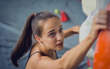 Güçlü bir dişi tırmanıcı renkli tutacakları ve ipleriyle yapay bir duvara tırmanır.