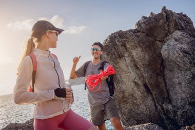 Genç çift, okyanus kıyısındaki dağların zirvesine bir iple tırmanır..