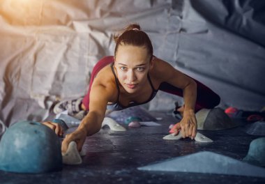 Güçlü bir dişi tırmanıcı renkli tutacakları ve ipleriyle yapay bir duvara tırmanır.