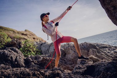 İpi olan genç bir kadın okyanusun yanındaki dağların tepesine tırmanır..