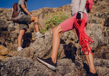 Genç çift, okyanus kıyısındaki dağların zirvesine bir iple tırmanır..