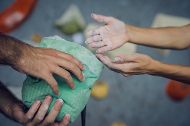 Birkaç dağcı renkli tutacakları ve ipleri olan yapay bir duvara tırmanmak için talk pudrası kullanıyor.