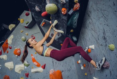 Güçlü bir dişi tırmanıcı renkli tutacakları ve ipleriyle yapay bir duvara tırmanır.