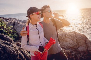 Genç çift, okyanus kıyısındaki dağların zirvesine bir iple tırmanır..