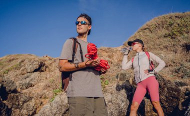 Genç çift, okyanus kıyısındaki dağların zirvesine bir iple tırmanır..