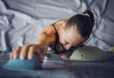 Güçlü bir dişi tırmanıcı renkli tutacakları ve ipleriyle yapay bir duvara tırmanır.