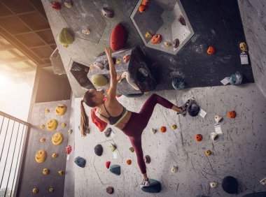 Güçlü bir dişi tırmanıcı renkli tutacakları ve ipleriyle yapay bir duvara tırmanır.