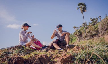 Mutlu genç çift okyanus kıyısındaki dağların tepesine tırmandıktan sonra rahatlıyor..