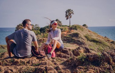 Mutlu genç çift okyanus kıyısındaki dağların tepesine tırmandıktan sonra rahatlıyor..