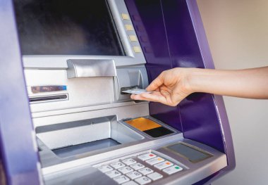 Genç bir kadın ATM 'den para çekmek için kartı kullanıyor..