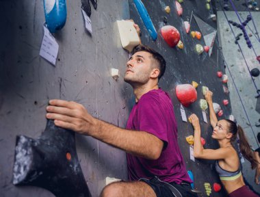 Güçlü bir çift tırmanışçı renkli tutacakları ve ipleriyle yapay bir duvara tırmanıyor.