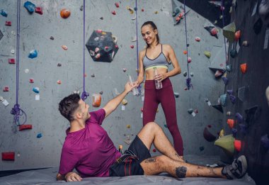 Güçlü bir çift tırmanışçı renkli tutacakları ve ipleriyle yapay duvarın yanında rahatlar.