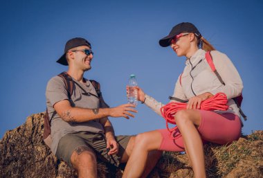 Mutlu genç çift okyanus kıyısındaki dağların tepesine tırmandıktan sonra rahatlıyor..