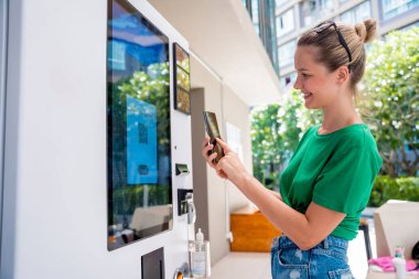 Otomatta kahve parasını ödeyen genç bir kadın. Temassız ödeme yöntemi kullanıyor..