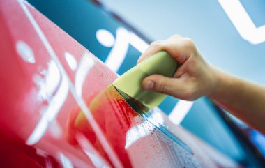 Yeni kırmızı arabaya koruyucu film yükleme işlemi