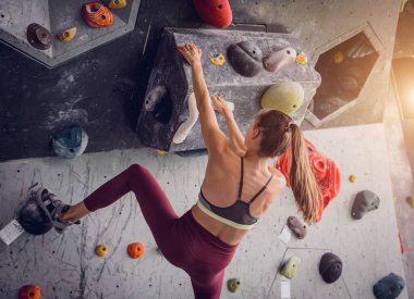 Güçlü bir dişi tırmanıcı renkli tutacakları ve ipleriyle yapay bir duvara tırmanır.