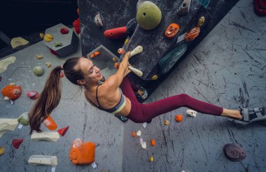 Güçlü bir dişi tırmanıcı renkli tutacakları ve ipleriyle yapay bir duvara tırmanır.