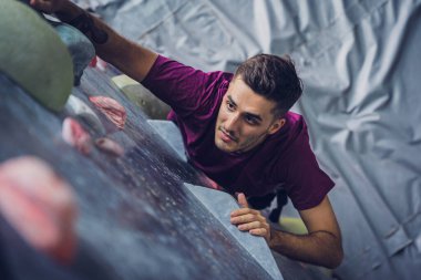 Güçlü bir erkek tırmanıcı renkli tutacakları ve ipleriyle yapay bir duvara tırmanır.