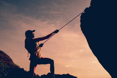 İpi olan genç bir kadın okyanusun yanındaki dağların tepesine tırmanır..