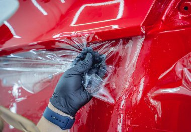 Araba servisindeki işçiler koruyucu film uygulamadan önce arabaya su sıkarlar.