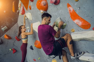 Güçlü bir çift tırmanışçı renkli tutacakları ve ipleriyle yapay bir duvara tırmanıyor.