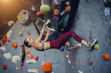 Güçlü bir dişi tırmanıcı renkli tutacakları ve ipleriyle yapay bir duvara tırmanır.