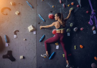 Güçlü bir dişi tırmanıcı renkli tutacakları ve ipleriyle yapay bir duvara tırmanır.