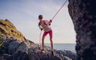 İpi olan genç bir kadın okyanusun yanındaki dağların tepesine tırmanır..