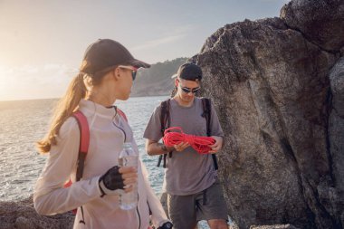 Genç çift, okyanus kıyısındaki dağların zirvesine bir iple tırmanır..